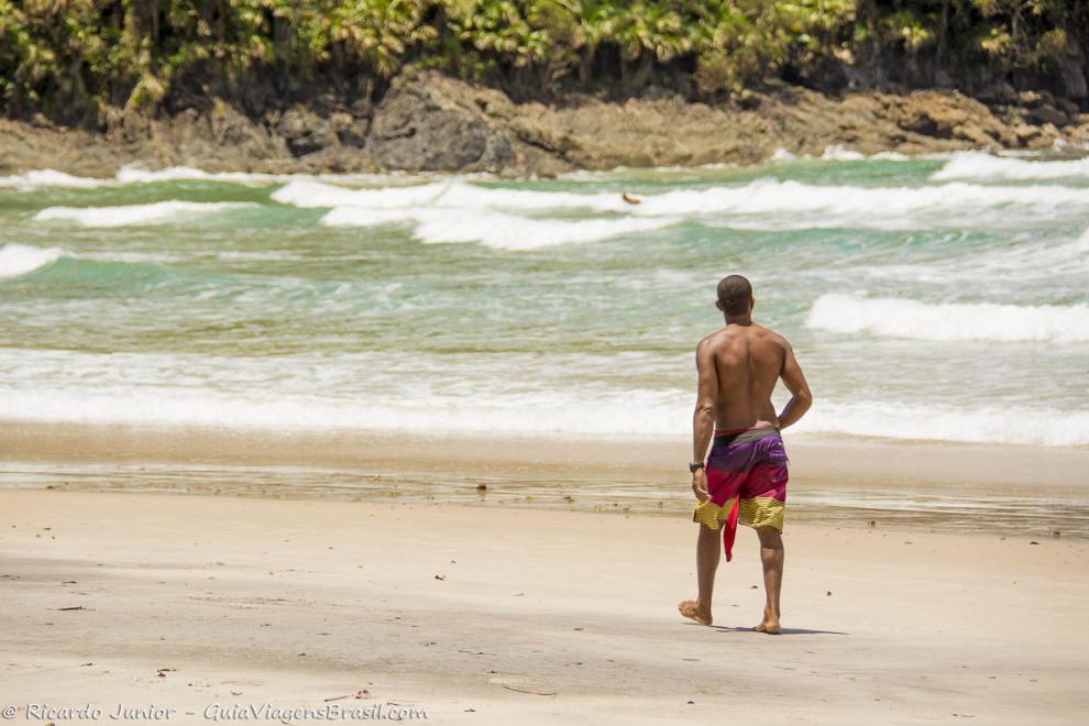Imagem de um rapaz andando na beira do mar da Praia da Engenhoca.